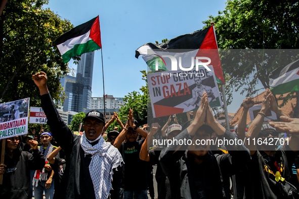 Muslims hold up posters during a pro-Palestinian rally on the eve of the one-year anniversary of the Israel-Hamas conflict in Surabaya, Indo...