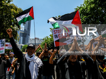 Muslims hold up posters during a pro-Palestinian rally on the eve of the one-year anniversary of the Israel-Hamas conflict in Surabaya, Indo...