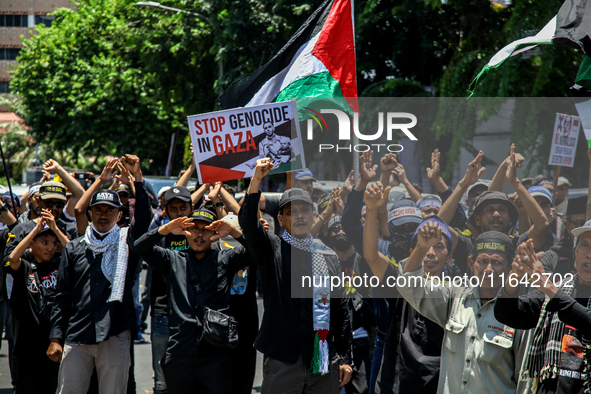 Muslims hold up posters during a pro-Palestinian rally on the eve of the one-year anniversary of the Israel-Hamas conflict in Surabaya, Indo...