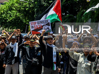 Muslims hold up posters during a pro-Palestinian rally on the eve of the one-year anniversary of the Israel-Hamas conflict in Surabaya, Indo...