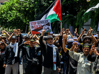 Muslims hold up posters during a pro-Palestinian rally on the eve of the one-year anniversary of the Israel-Hamas conflict in Surabaya, Indo...