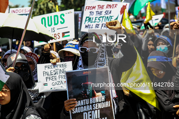 Muslims hold up posters during a pro-Palestinian rally on the eve of the one-year anniversary of the Israel-Hamas conflict in Surabaya, Indo...