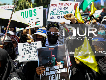 Muslims hold up posters during a pro-Palestinian rally on the eve of the one-year anniversary of the Israel-Hamas conflict in Surabaya, Indo...