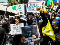 Muslims hold up posters during a pro-Palestinian rally on the eve of the one-year anniversary of the Israel-Hamas conflict in Surabaya, Indo...