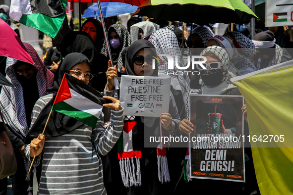 Muslims hold up posters during a pro-Palestinian rally on the eve of the one-year anniversary of the Israel-Hamas conflict in Surabaya, Indo...