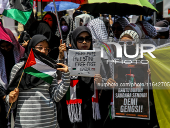 Muslims hold up posters during a pro-Palestinian rally on the eve of the one-year anniversary of the Israel-Hamas conflict in Surabaya, Indo...