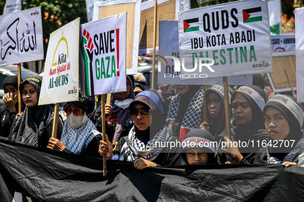 Muslims hold up posters during a pro-Palestinian rally on the eve of the one-year anniversary of the Israel-Hamas conflict in Surabaya, Indo...