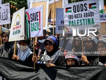 Muslims hold up posters during a pro-Palestinian rally on the eve of the one-year anniversary of the Israel-Hamas conflict in Surabaya, Indo...