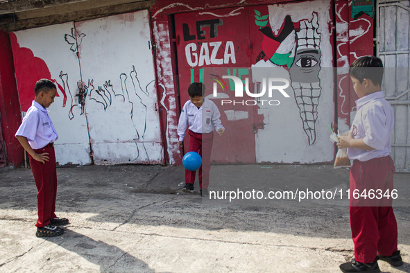 Students play football in front of a mural supporting the Palestinian people on a wall in the Liogenteng settlement area in Bandung, West Ja...