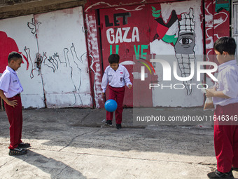 Students play football in front of a mural supporting the Palestinian people on a wall in the Liogenteng settlement area in Bandung, West Ja...