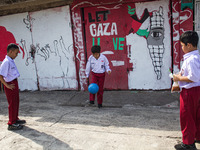 Students play football in front of a mural supporting the Palestinian people on a wall in the Liogenteng settlement area in Bandung, West Ja...