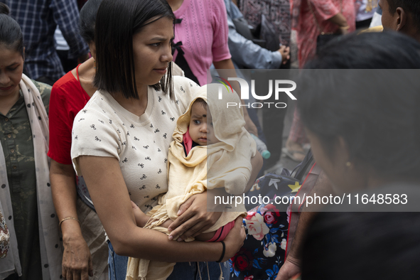 A woman with her infant stands in the crowd of people shopping at a street market ahead of the Durga Puja festival in Guwahati, India, on Oc...