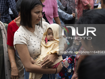 A woman with her infant stands in the crowd of people shopping at a street market ahead of the Durga Puja festival in Guwahati, India, on Oc...