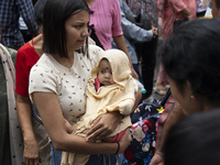 A woman with her infant stands in the crowd of people shopping at a street market ahead of the Durga Puja festival in Guwahati, India, on Oc...