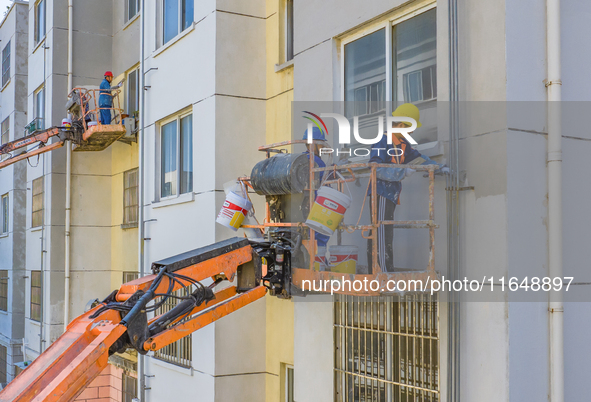 Workers paint the exterior walls of an old residential area at the renovation site in Suqian, Jiangsu province, China, on October 8, 2024. 