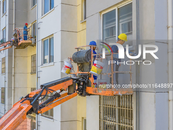 Workers paint the exterior walls of an old residential area at the renovation site in Suqian, Jiangsu province, China, on October 8, 2024. (