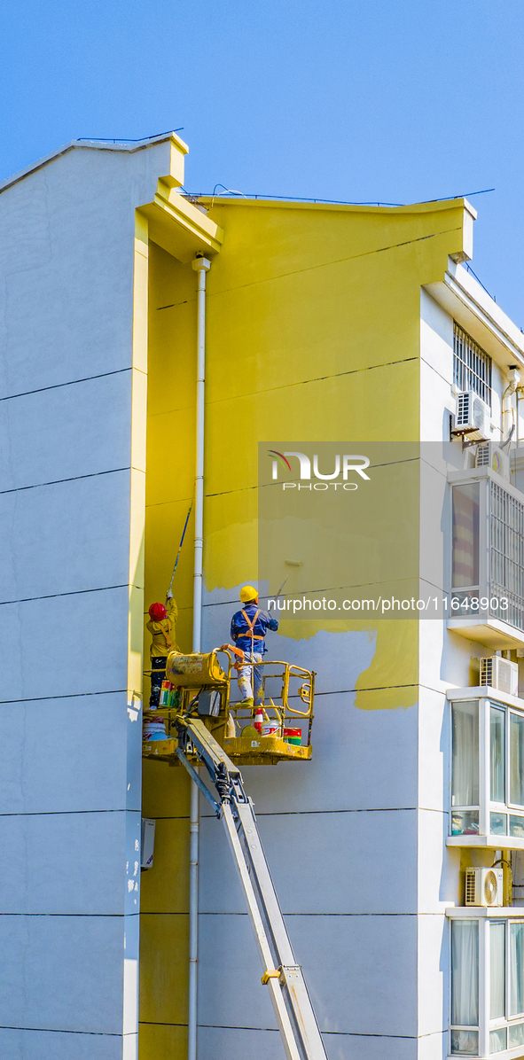 Workers paint the exterior walls of an old residential area at the renovation site in Suqian, Jiangsu province, China, on October 8, 2024. 