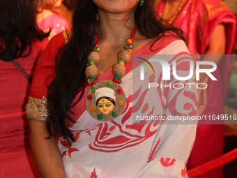 A Bengali Hindu woman wears a necklace with an image of the Goddess Durga while waiting to offer prayers during the Durga Puja festival at a...