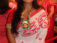 A Bengali Hindu woman wears a necklace with an image of the Goddess Durga while waiting to offer prayers during the Durga Puja festival at a...