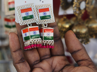 A woman looks at a pair of earrings decorated with the flag of India at a small stall selling costume jewelry and temple jewelry during the...