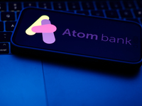 A laptop keyboard and Atom Bank logo displayed on a phone screen are seen in this illustration photo taken in Poland on October 8, 2024. (