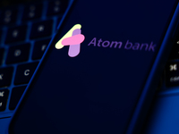 A laptop keyboard and Atom Bank logo displayed on a phone screen are seen in this illustration photo taken in Poland on October 8, 2024. (