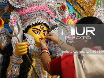 A Hindu married woman puts on a gold nose ring as part of rituals before she offers prayer to an idol of the Hindu goddess Durga inside a 18...