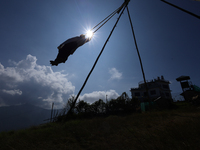 A Nepali woman is silhouetted against the sun as she plays on a swing installed on a hillside surrounding Kathmandu Valley with the arrival...