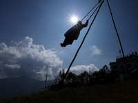 A Nepali woman is silhouetted against the sun as she plays on a swing installed on a hillside surrounding Kathmandu Valley with the arrival...