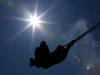 A Nepali man is silhouetted against the sun as he plays on a swing installed on a hillside surrounding Kathmandu Valley in Nepal, on October...