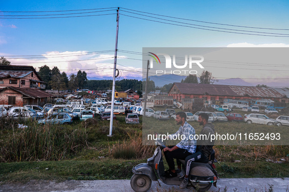 Kashmiri boys ride a scooter as seized and damaged vehicles are seen inside a yard on the outskirts of Srinagar, Jammu and Kashmir, India, o...