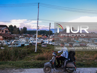 Kashmiri boys ride a scooter as seized and damaged vehicles are seen inside a yard on the outskirts of Srinagar, Jammu and Kashmir, India, o...