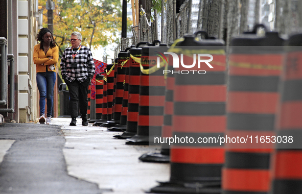 Pedestrians walk beside construction traffic barrels along Queen Street in downtown Brampton, Ontario, Canada, on October 9, 2024, after a l...