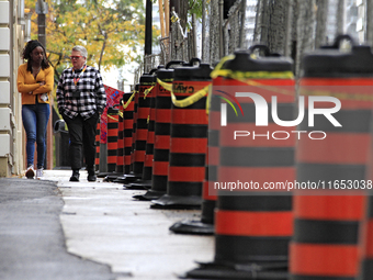 Pedestrians walk beside construction traffic barrels along Queen Street in downtown Brampton, Ontario, Canada, on October 9, 2024, after a l...