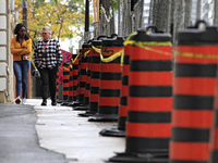 Pedestrians walk beside construction traffic barrels along Queen Street in downtown Brampton, Ontario, Canada, on October 9, 2024, after a l...