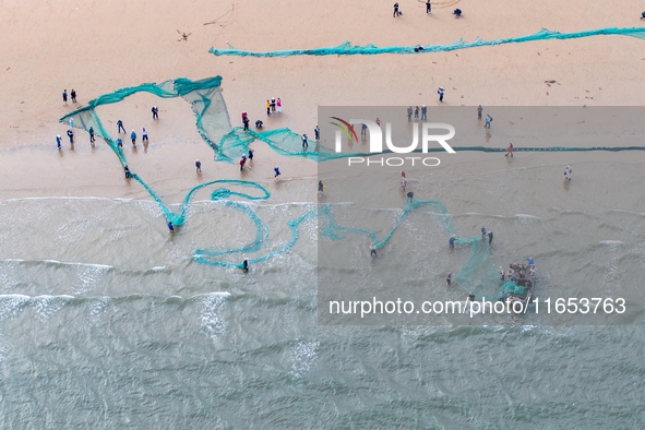 Fishermen cast long nets to catch seafood at the shore of the Yellow Sea in Lingshan Bay, West Coast New District, in Qingdao, China, on Oct...