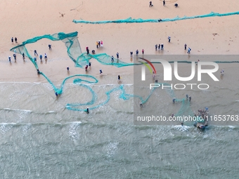 Fishermen cast long nets to catch seafood at the shore of the Yellow Sea in Lingshan Bay, West Coast New District, in Qingdao, China, on Oct...