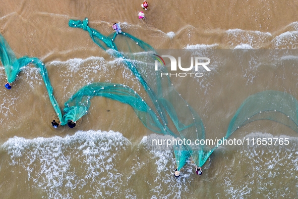 Fishermen cast long nets to catch seafood at the shore of the Yellow Sea in Lingshan Bay, West Coast New District, in Qingdao, China, on Oct...