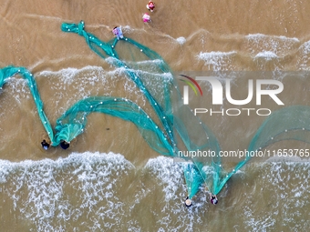 Fishermen cast long nets to catch seafood at the shore of the Yellow Sea in Lingshan Bay, West Coast New District, in Qingdao, China, on Oct...