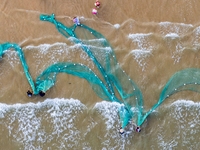 Fishermen cast long nets to catch seafood at the shore of the Yellow Sea in Lingshan Bay, West Coast New District, in Qingdao, China, on Oct...