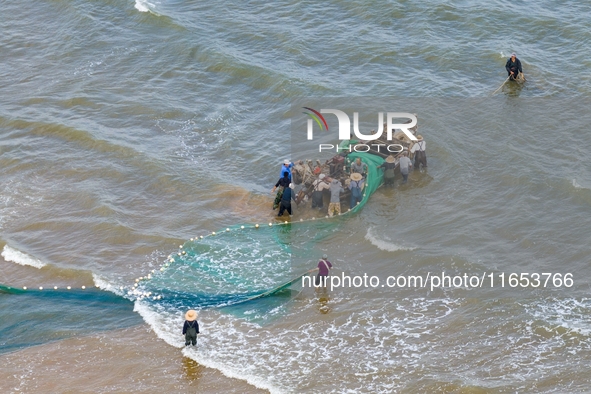 Fishermen cast long nets to catch seafood at the shore of the Yellow Sea in Lingshan Bay, West Coast New District, in Qingdao, China, on Oct...