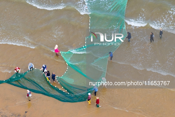 Fishermen cast long nets to catch seafood at the shore of the Yellow Sea in Lingshan Bay, West Coast New District, in Qingdao, China, on Oct...