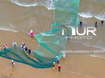 Fishermen cast long nets to catch seafood at the shore of the Yellow Sea in Lingshan Bay, West Coast New District, in Qingdao, China, on Oct...