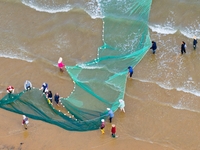 Fishermen cast long nets to catch seafood at the shore of the Yellow Sea in Lingshan Bay, West Coast New District, in Qingdao, China, on Oct...