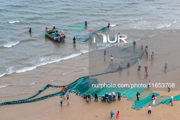 Fishermen cast long nets to catch seafood at the shore of the Yellow Sea in Lingshan Bay, West Coast New District, in Qingdao, China, on Oct...