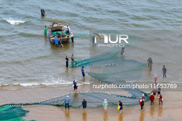 Fishermen cast long nets to catch seafood at the shore of the Yellow Sea in Lingshan Bay, West Coast New District, in Qingdao, China, on Oct...