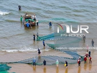 Fishermen cast long nets to catch seafood at the shore of the Yellow Sea in Lingshan Bay, West Coast New District, in Qingdao, China, on Oct...