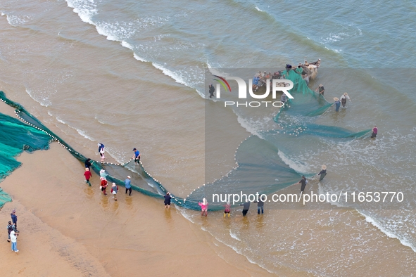 Fishermen cast long nets to catch seafood at the shore of the Yellow Sea in Lingshan Bay, West Coast New District, in Qingdao, China, on Oct...