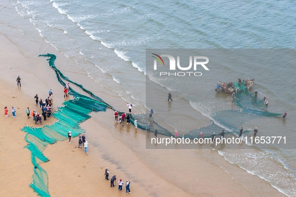 Fishermen cast long nets to catch seafood at the shore of the Yellow Sea in Lingshan Bay, West Coast New District, in Qingdao, China, on Oct...