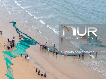 Fishermen cast long nets to catch seafood at the shore of the Yellow Sea in Lingshan Bay, West Coast New District, in Qingdao, China, on Oct...